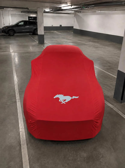 Ford Mustang protected by a red precision-fit indoor car cover, viewed from above